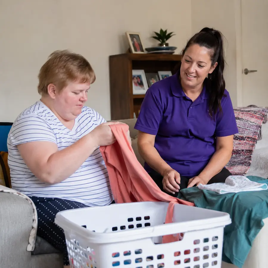 SIL participant folding her clothes and support worker is guidig her